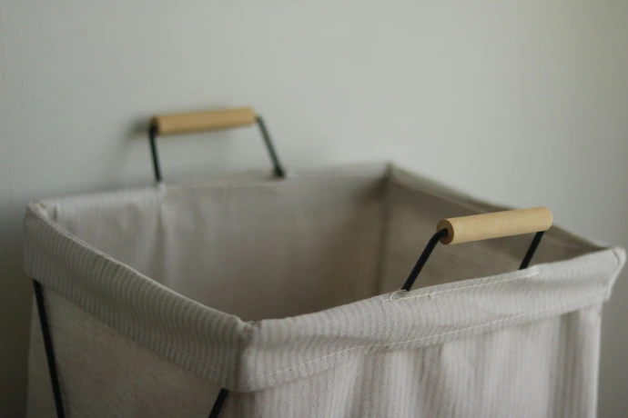 An empty, light-colored laundry hamper with wooden handles